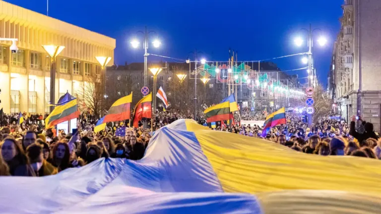 Didelė minia žmonių laiko Ukrainos vėliavą gatvėje su Lietuvos vėliavomis vakare Vilniuje.