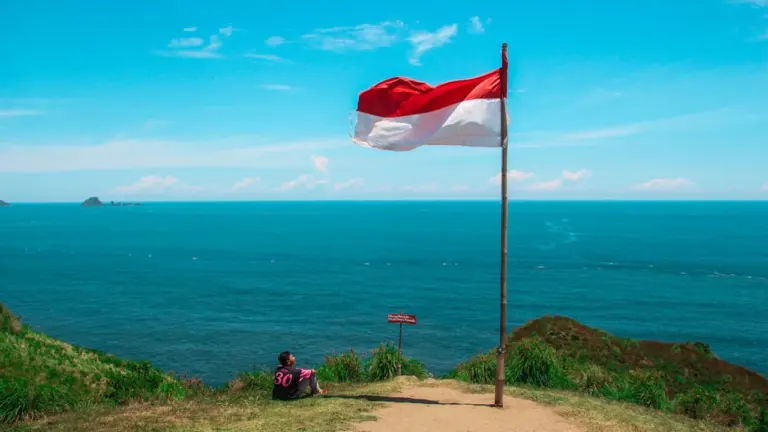 Indonezijos vėliava plevėsuoja paplūdimio fone, simbolizuojanti šalies nepriklausomybės dvasią ir gamtos grožį.