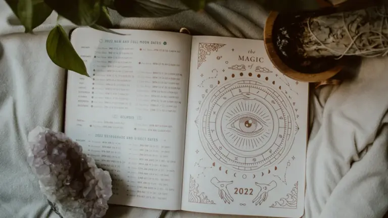 Atversta knyga su astrologiniais simboliais, kristalu ir augalu ramiam vakarui.