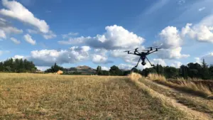 Juodas dronas skrenda virš atviro Lietuvos lauko giedrą vasaros dieną