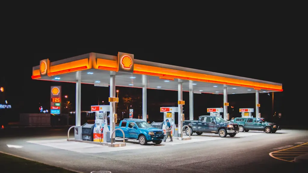 Degalinės stotis su automobiliais dienos metu, atspindinti kasdienes vairuotojų išlaidas degalams.