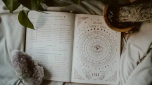 Atverta knyga su astrologiniais ženklais, kristalais ir ramiu rudenišku fonu.