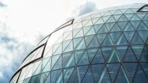 Moderni savivaldybės pastato stiklinė architektūra dangaus fone, simbolizuojanti skaidrumą ir atvirumą.